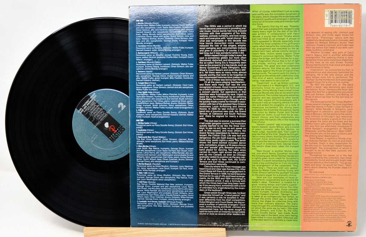 A vinyl record partially pulled from its back cover, showing a black record on the left and a colorful printed back cover with blue, black, green, and peach sections on the right.