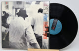 A vinyl record partially pulled from its sleeve, showing the black disc and the album cover with a black-and-white photo and vertical red text reading 'FREDERICK BINGHAMS HARRY Mudditt.'.