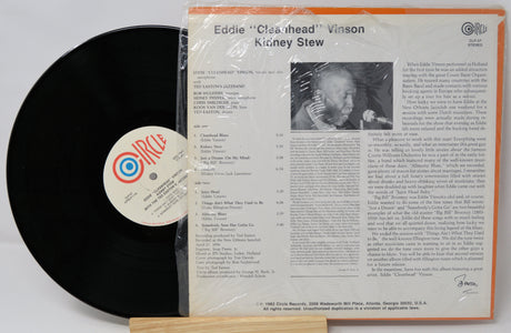 Vinyl record with cover featuring text and a photo of a person, on a white background