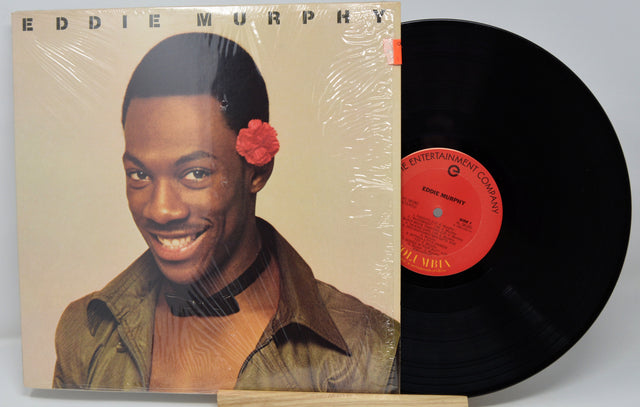 Vinyl record with cover featuring a smiling man with a flower in his hair, on a beige background.