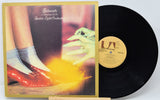 Vinyl record with cover featuring a person in red shoes and gray socks, on a white background.
