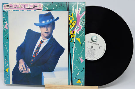 Vinyl record with cover featuring a person in a blue suit and hat, on a light gray background.