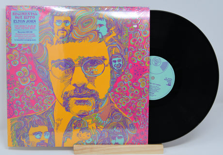 Vinyl record with a colorful cover featuring a portrait of a young Elton John with glasses on a light gray background