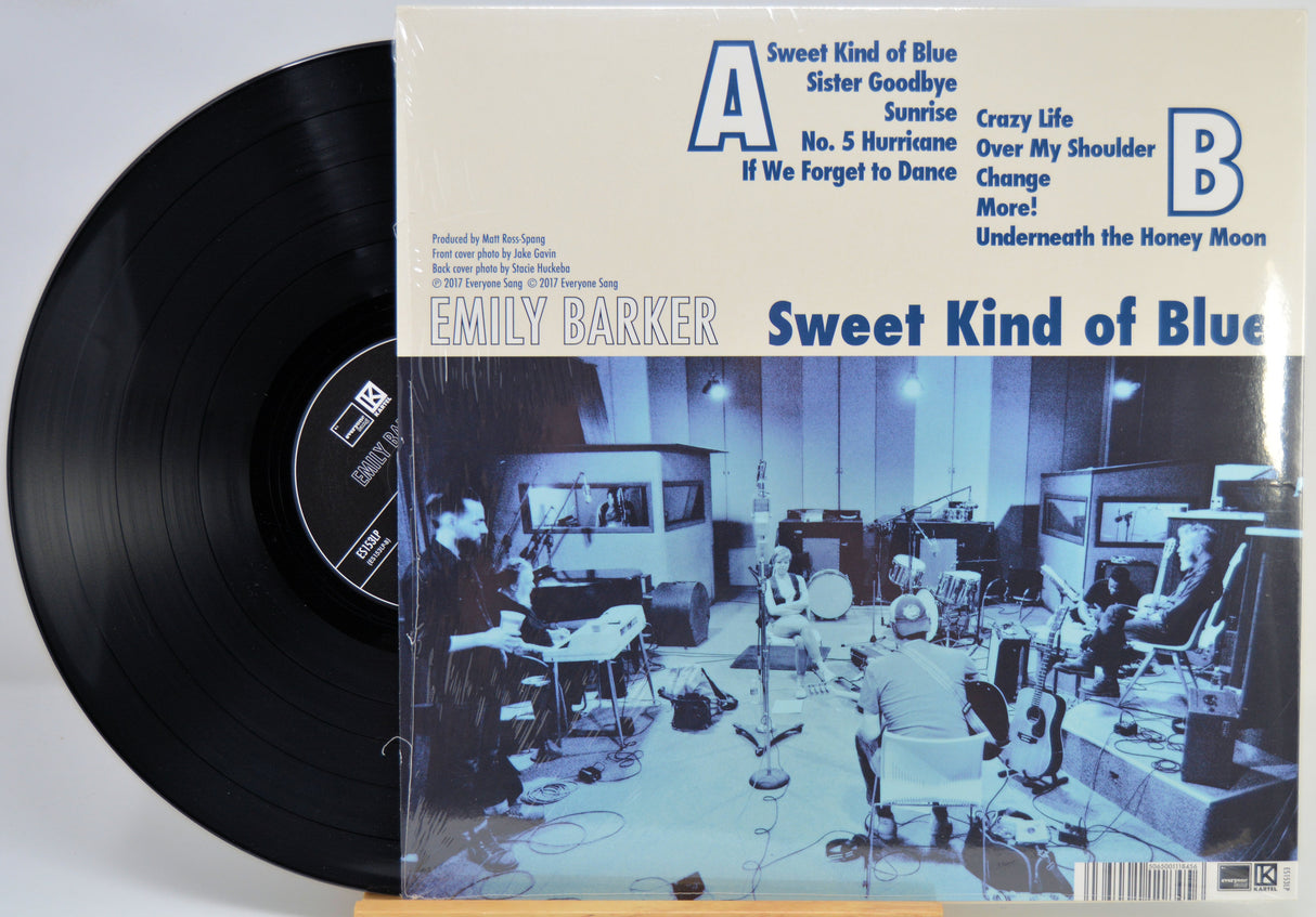 A vinyl record partially pulled from its sleeve, showing the black disc on the left and the album cover on the right. The cover reads 'EMILY BARKER Sweet Kind of Blue' with track listings and a blue-toned studio photo.