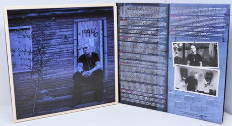 Eminem sitting on steps outside a boarded house with 19946 on the door, album inner art