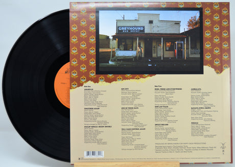 Vinyl record album shown with the black LP partially pulled from the back cover, which features a photo of a storefront building labeled 'GREYHOUND BUS STOP' and track listing text on a beige background.