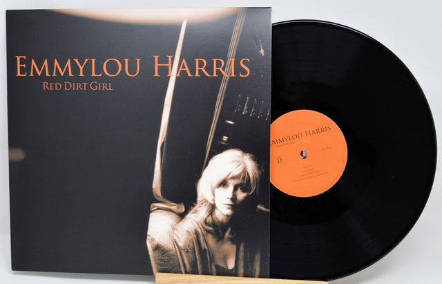 Emmylou Harris 'Red Dirt Girl' vinyl record LP with the album cover partially obscuring the black record and an orange center label, photographed on a light neutral background.