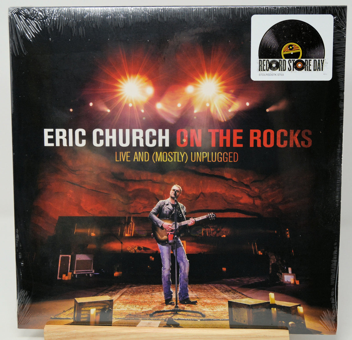 Eric Church 'On the Rocks' vinyl record cover, sealed in shrink wrap, displayed on a wooden stand against a white background. The cover features a live performance scene with stage lights and a Record Store Day badge in the top right corner.