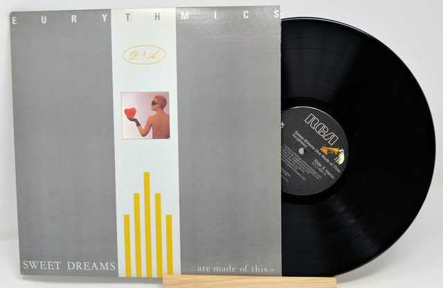 Eurythmics - Sweet Dreams album cover and vinyl record. The cover features a gray background with yellow and white stripes and a silhouette of a person holding a heart.
