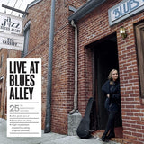 Woman standing in the doorway of a brick building with 'Blues Alley' sign, promotional poster for 'Live at Blues Alley' on left.
