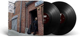 Two vinyl records with a person standing in front of a brick building with a 'Blue' sign.