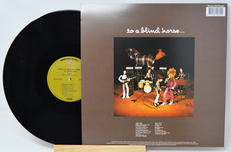 A vinyl record partially pulled from its album sleeve, showing the black record on the left and the brown cover on the right with the title 'to a blind horse.