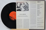 Vinyl record with a black label and a record cover featuring text and a photo of people.
