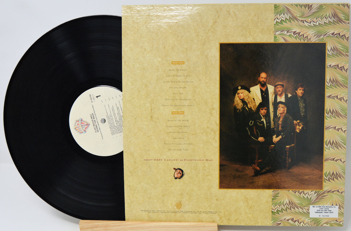 A vinyl record partially pulled from its sleeve, showing the black record on the left and the beige album cover on the right with a printed group portrait and decorative border.