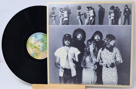 A black vinyl record partially pulled from its sleeve, showing the front cover artwork with a black-and-white band photo and a small multicolor label on the record, displayed on a wooden stand against a white background.