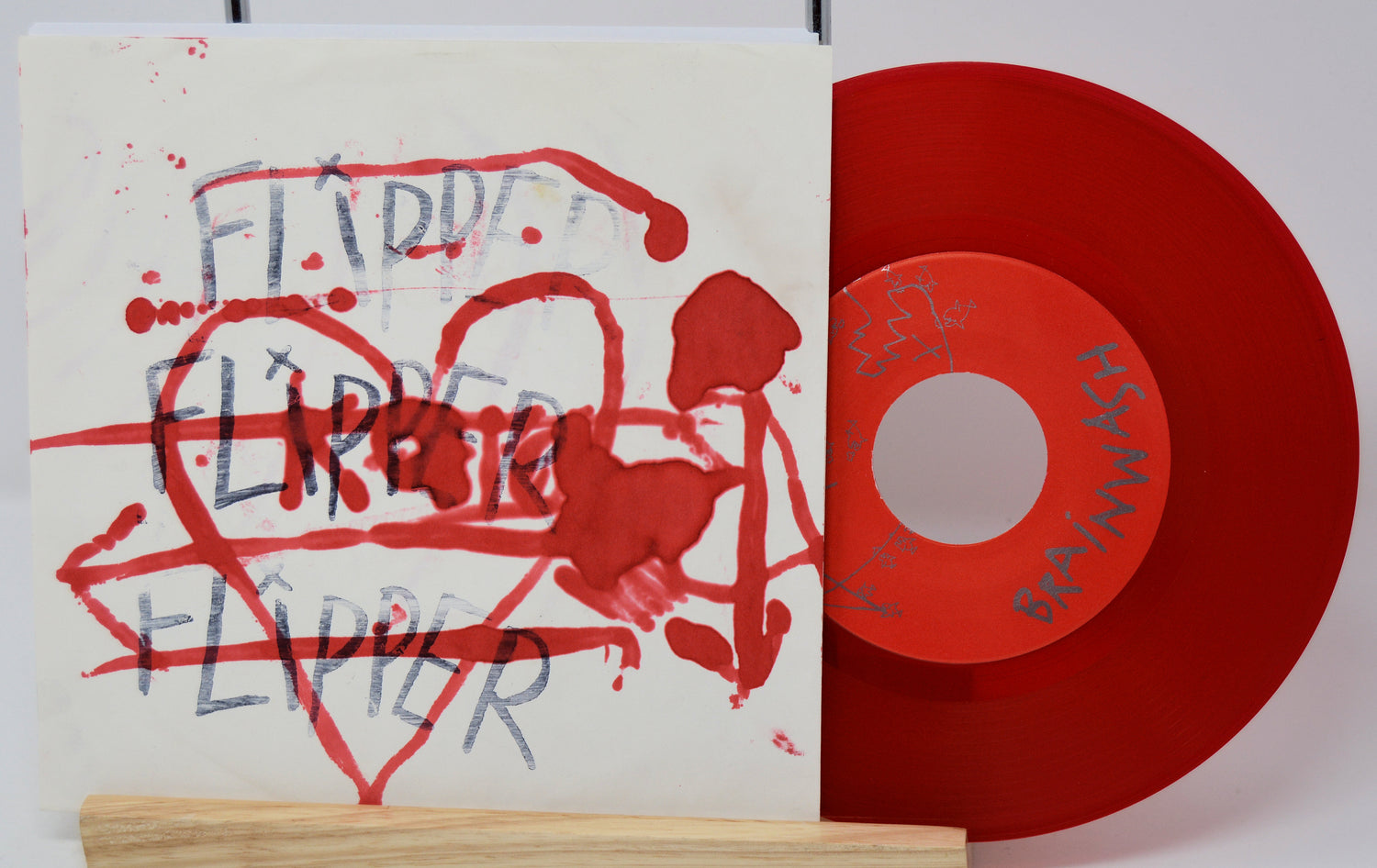 Red vinyl record with a white label and a sleeve featuring red and black text and graphics.