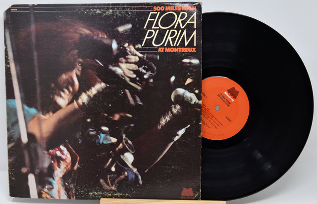 Vinyl record album '500 Miles from Hell' by Flora Purim, showing the illustrated cover on the left and the black record partially pulled out on the right against a light gray background.