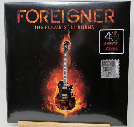 Foreigner - The Flame Still Burns vinyl record album cover, featuring a black electric guitar engulfed in flames on a black background, with a 40th anniversary sticker and a Resonance Store Day sticker on the right.