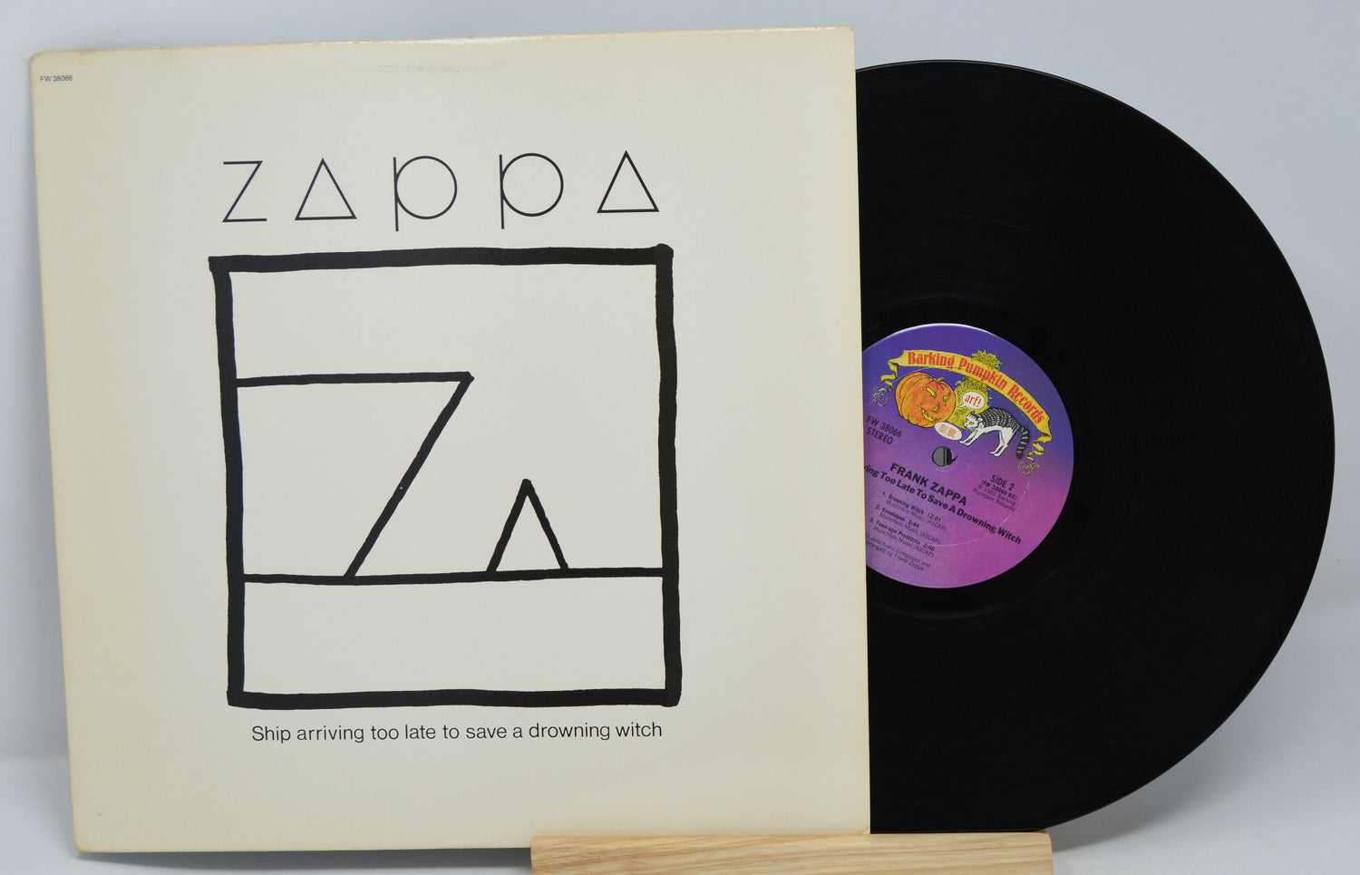 A vinyl record and its cover with the text 'Zappa' and 'Ship Arriving Too Late To Save Drowning Witch' on the cover. The record is black with a purple label.