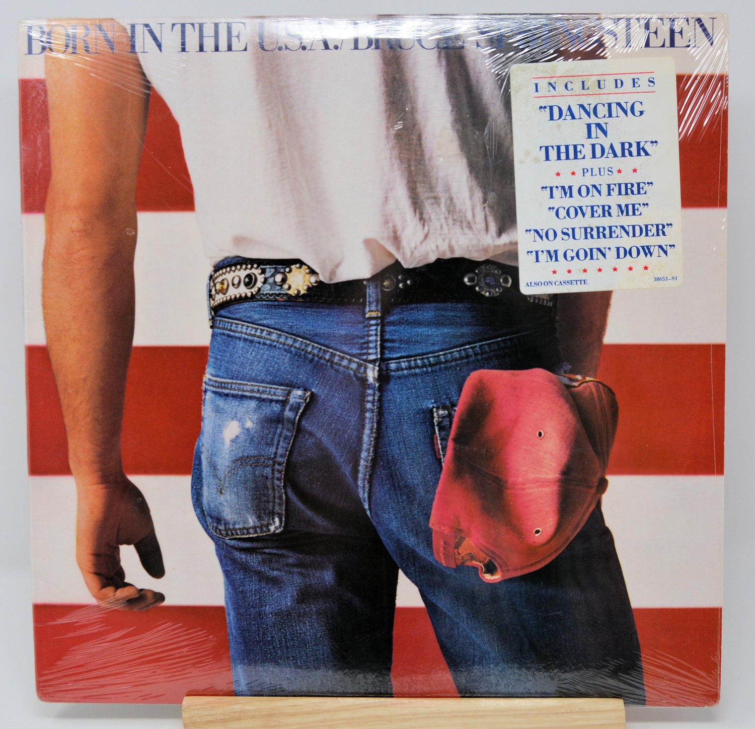 Front cover of 'Born in the U.S.A.' vinyl album with denim jeans, a white shirt, red cap, and a sticker listing hit songs