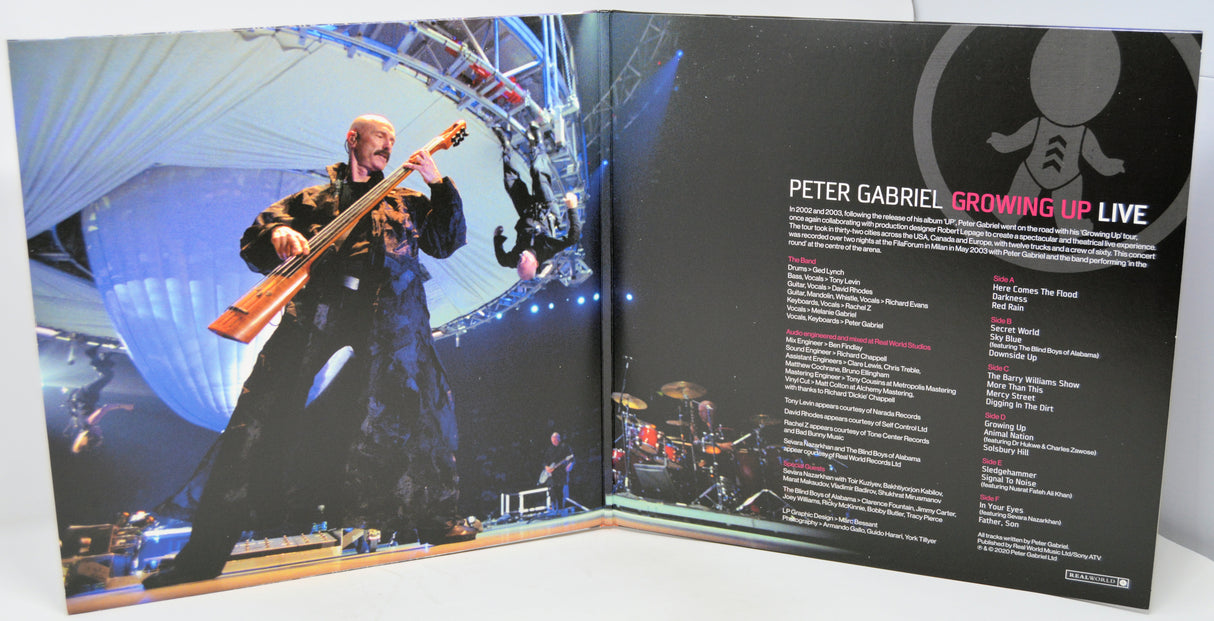 Open book showing a live performance image of a musician playing bass and album cover details for 'Growing Up Live' by Peter Gabriel.