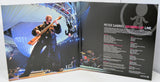 Open book showing a live performance image of a musician playing bass and album cover details for 'Growing Up Live' by Peter Gabriel.