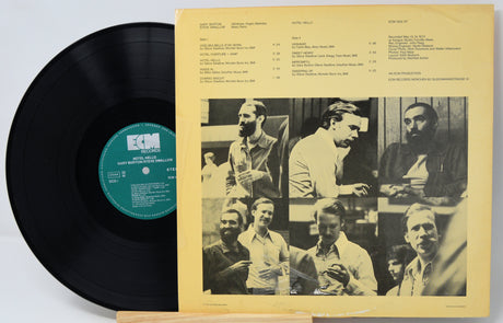 A vinyl record partially pulled from its sleeve, showing the black record with a green ECM label next to the cream-colored inner cover featuring black-and-white photos and printed text.