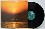 A vinyl record album with its cover partially pulled from the sleeve, showing a sunset seascape artwork. The black LP record is partially visible behind the cover, and the center label reads ECM.