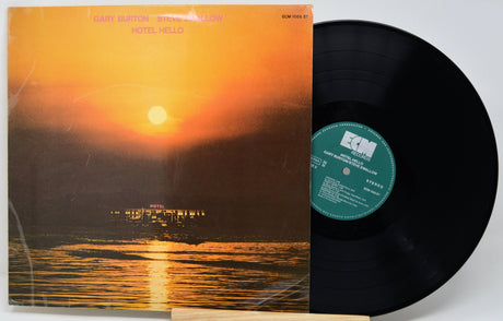 A vinyl record album with its cover partially pulled from the sleeve, showing a sunset seascape artwork. The black LP record is partially visible behind the cover, and the center label reads ECM.