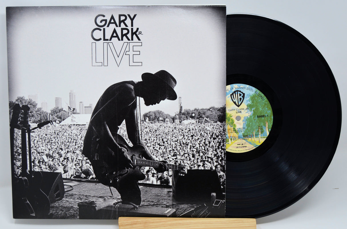 A vinyl record titled 'Gary Clark Jr Live' with an image of a man playing a guitar on the cover, in front of a crowd. The record is on a white background.