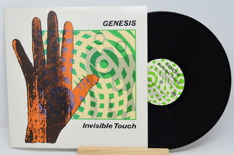 A vinyl record of the album 'Invisible Touch' by Genesis, featuring a hand illustration and geometric patterns on the cover.