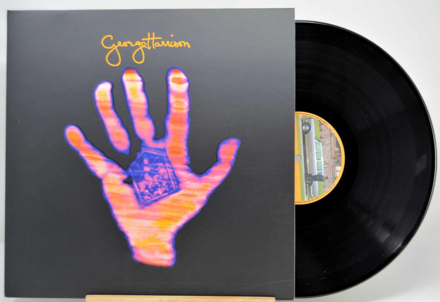 A vinyl record partially pulled from its sleeve, showing the album cover artwork with a large stylized hand in pink, orange, and blue on a dark background, and the black record disc visible behind it.
