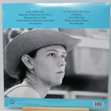 Back cover of a vinyl record sleeve featuring a black-and-white portrait of a woman in a cowboy hat, with a bright blue band at the top listing track titles and a barcode at the bottom.