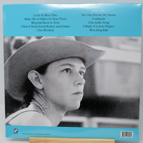Back cover of a vinyl record sleeve featuring a black-and-white portrait of a woman in a cowboy hat, with a bright blue band at the top listing track titles and a barcode at the bottom.