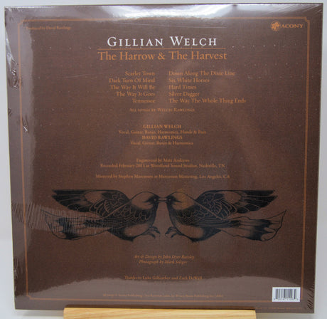 The back cover of Gillian Welch's 'The Harrow & The Harvest' vinyl record album on Acoustic Records, featuring a dark brown background with tracklist text and a black bird illustration.