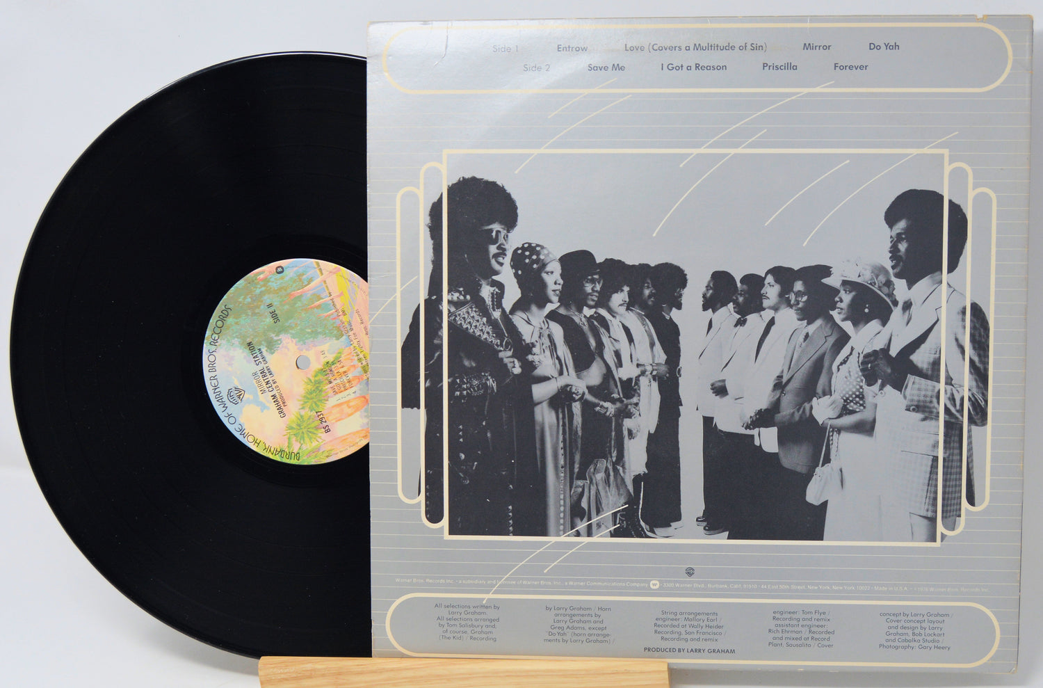 Vinyl record with a black cover and a gray inner sleeve featuring a group of people.