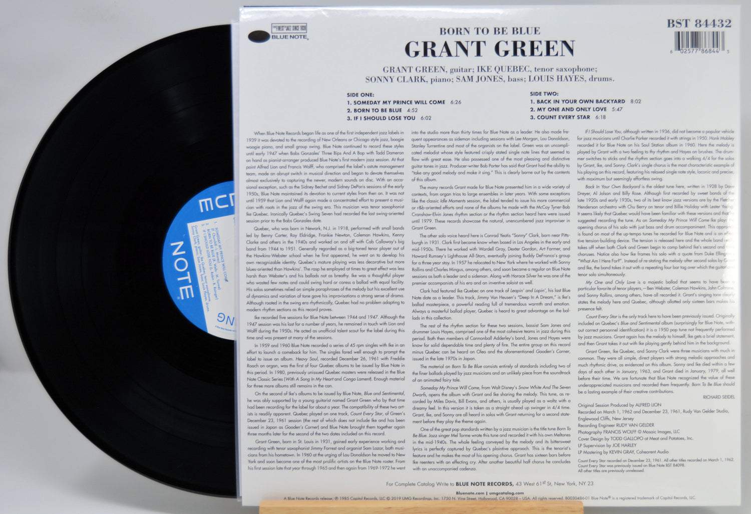 A vinyl record partially pulled from its back cover sleeve, showing the black record on the left and the printed back of the album case on the right. The cover reads 'Grant Green - Born to Be Blue' with track listing and copyright details.