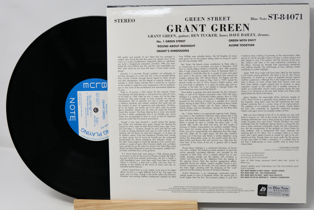 A vintage vinyl record album shown with the black record partially pulled from its white paper sleeve. The sleeve features the title 'GRANT GREEN - Green Street' and dense printed track information, with a blue circular label on the record.