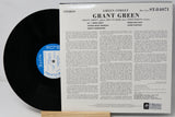 A vintage vinyl record album shown with the black record partially pulled from its white paper sleeve. The sleeve features the title 'GRANT GREEN - Green Street' and dense printed track information, with a blue circular label on the record.