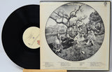 A vinyl record partially pulled from its sleeve, showing the black record on the left and the cream-colored album cover on the right with a large circular black-and-white band photograph and printed track listings.