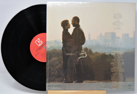 Vinyl record 'Grover Washington Jr Come Morning' with back cover featuring a couple and saxophone against a cityscape.