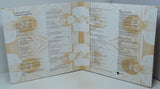 An open three-panel booklet or program spread, photographed from above on a light surface. The pages are predominantly white with beige/tan abstract line art and small circular photographic inserts, plus dense black text.