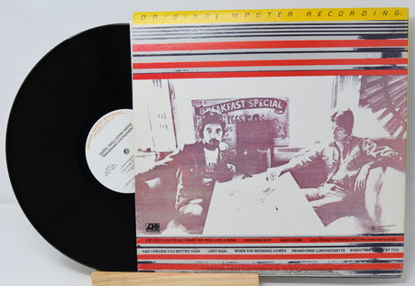 Vinyl record with a cover featuring two people and text, on a light gray background.