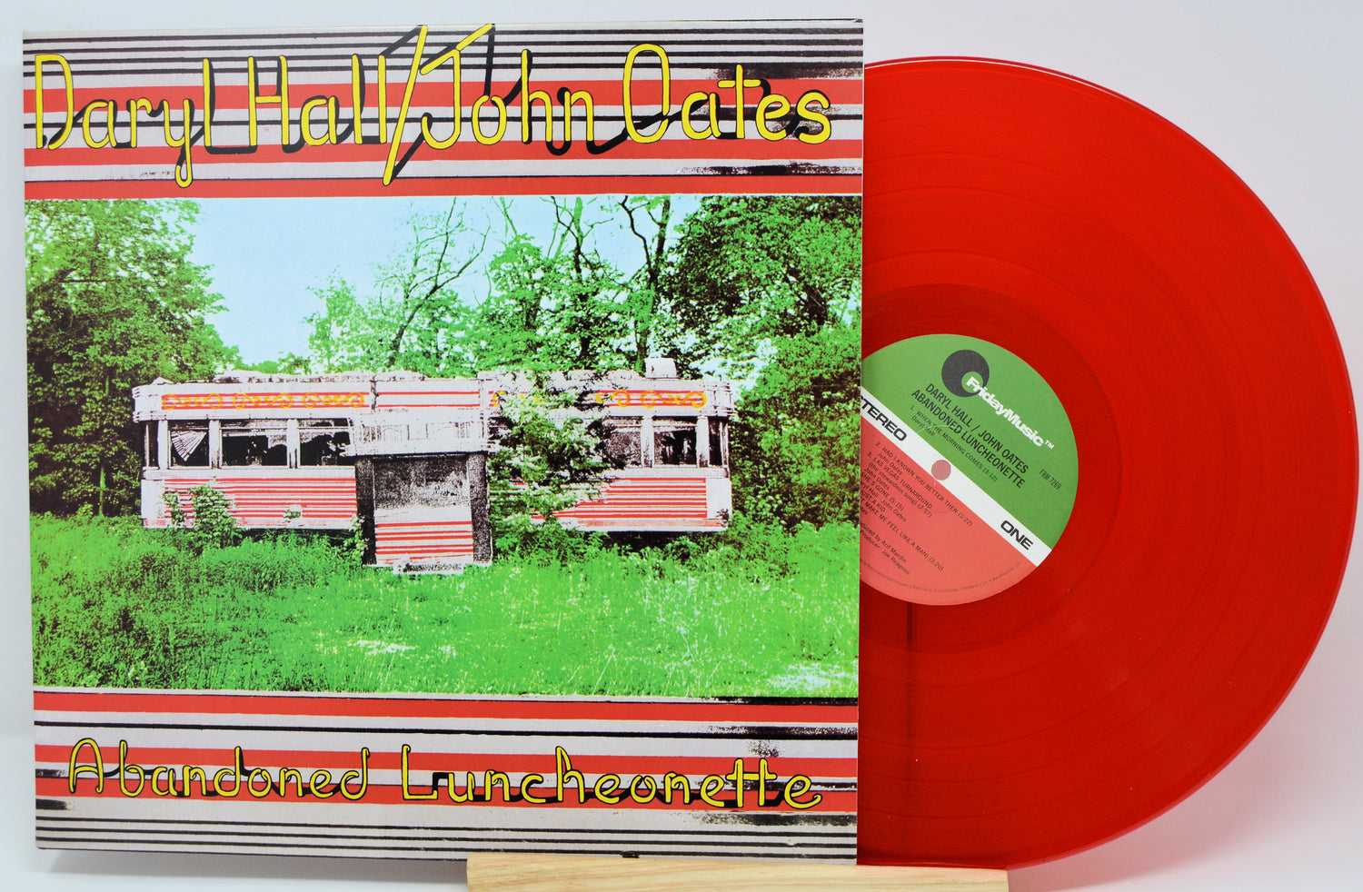 Vinyl record album cover for 'Abandoned Luncheonette' by Daryl Hall & John Oates, shown with a translucent red LP disc partially pulled out. The cover features a vintage red-and-white luncheonette in a grassy, tree-filled setting.