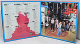 An open vinyl record album sleeve, likely a compilation or tribute album, displayed on a white surface. The left page features a white background with a large red silhouette of a person and a list of song titles and artists in black text, decorated with small blue and orange accents.