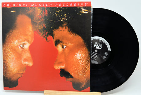 Vinyl record album with the cover partially pulled from its jacket, showing a black LP disc beside a square album cover featuring two men facing each other against a red background.