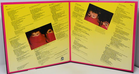 An open vinyl record sleeve or booklet with bright yellow printed pages, pink borders, and two small inset photos of a person in red clothing, photographed against a plain light background.