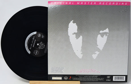 A vinyl record partially pulled from its sleeve, showing the black disc and the back cover artwork with a gray halftone face graphic and pink text reading 'Original Master Recording'.