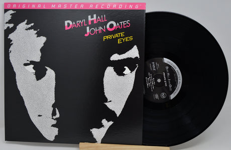 Vinyl record album for Daryl Hall & John Oates' 'Private Eyes' with the black record partially pulled from the sleeve, shown on a light gray background.