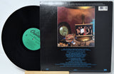 A vinyl record partially pulled from its album sleeve, showing the black record with a green label on the left and the back cover artwork on the right. The cover features a warm-toned photo of a band with track listing text below.